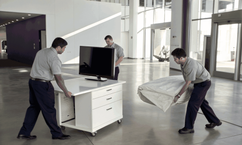 High‑resolution image of workers in black polo shirts and khaki pants removing office furniture from a Nepean commercial space, featuring a modern office interior and a clean truck in the background, styled with cool‑toned, crushed‑black grading.